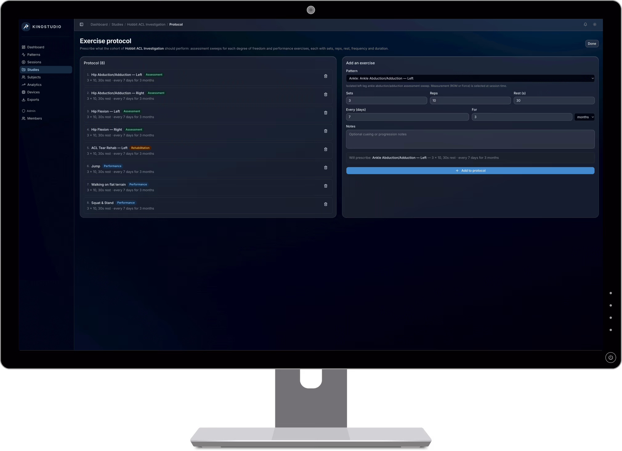KinoStudio exercise-protocol builder on a desktop monitor — every set, rep, rest interval and frequency locked into the prescribed protocol